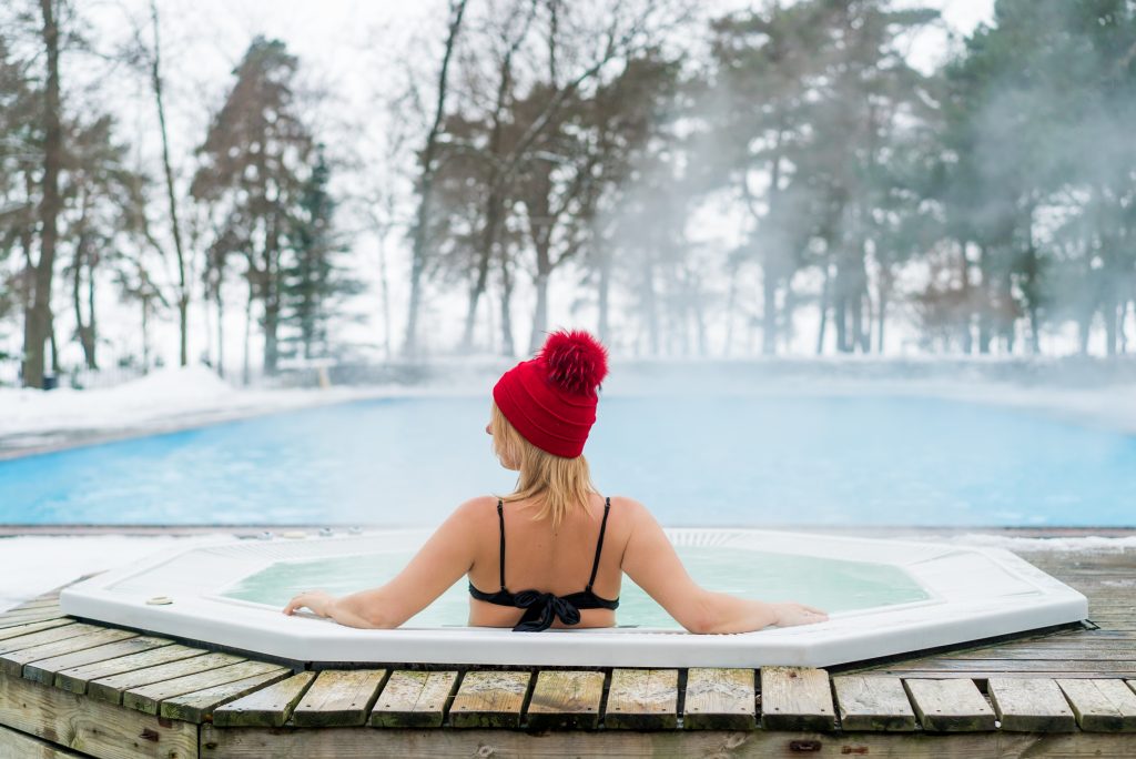 Young blonde woman in red hut in bathtub jacuzzi outdoors at winter day